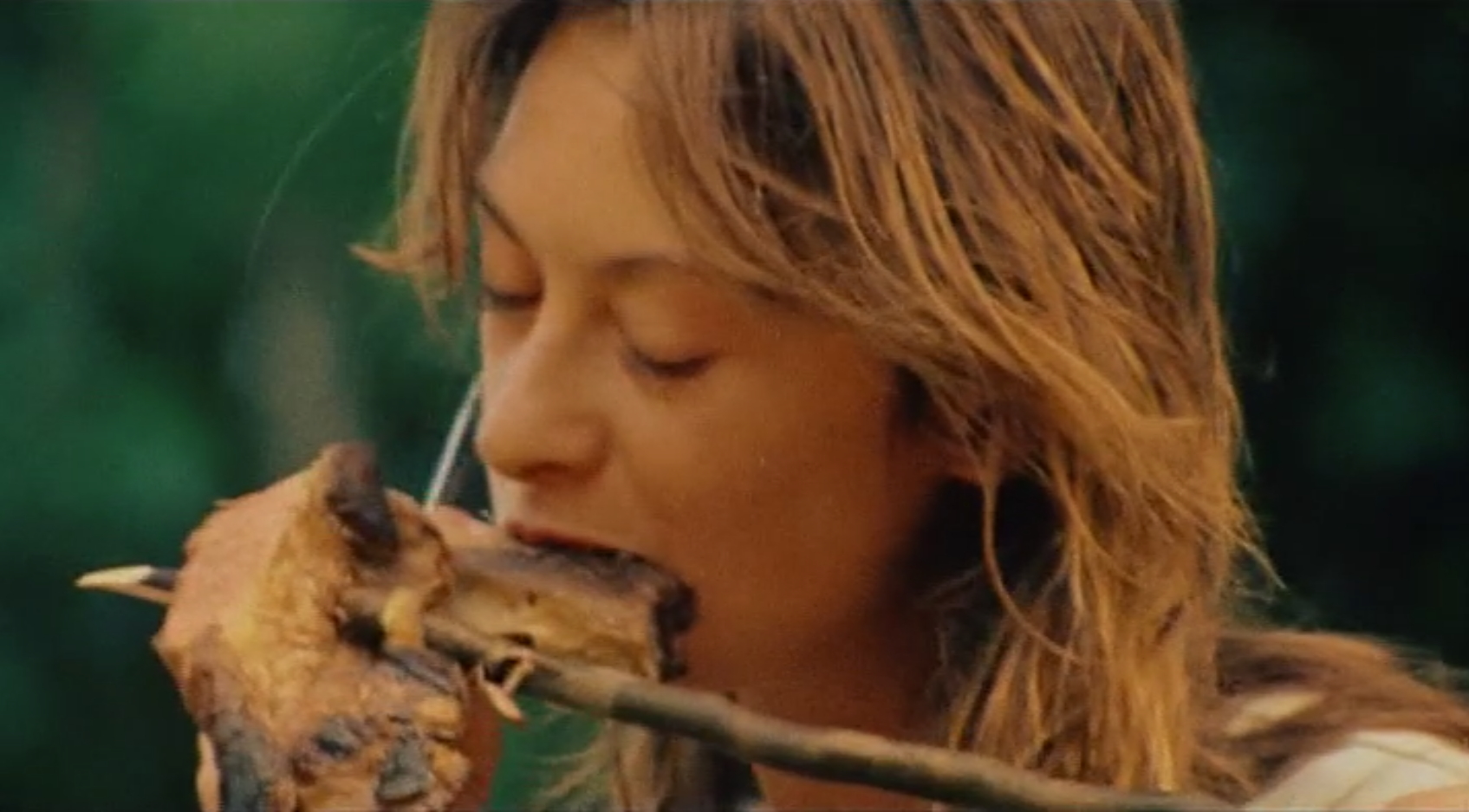 A still from <em<Cannibal Holocaust</em>: a character eats a piece of cooked tortoise meat on a stick